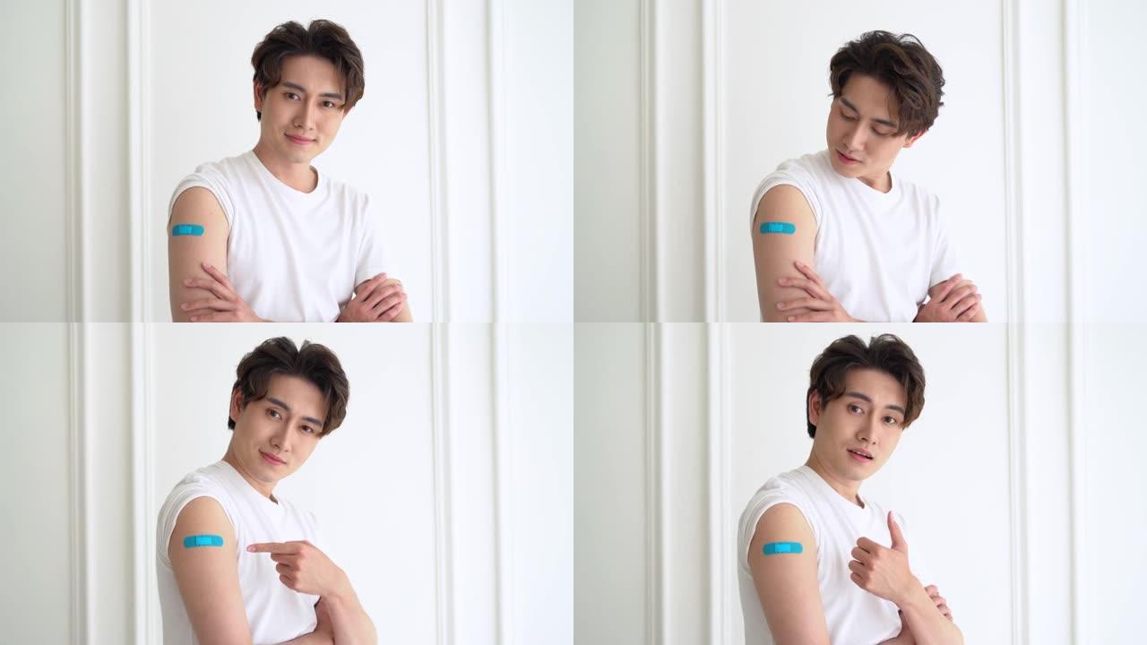 年轻的亚洲男子患者的肖像显示肩膀上的膏药表明注射后，用新型冠状病毒肺炎病毒接种疫苗后感到满意，并看着