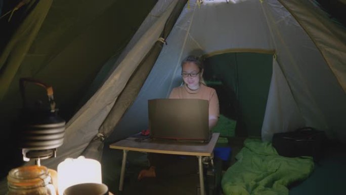 亚洲妇女晚上在帐篷里用笔记本电脑工作