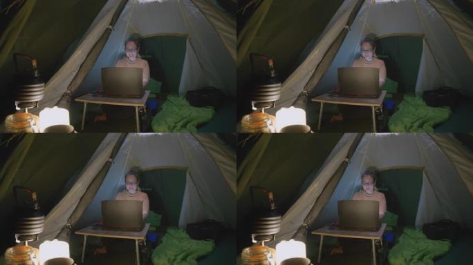亚洲妇女晚上在帐篷里用笔记本电脑工作