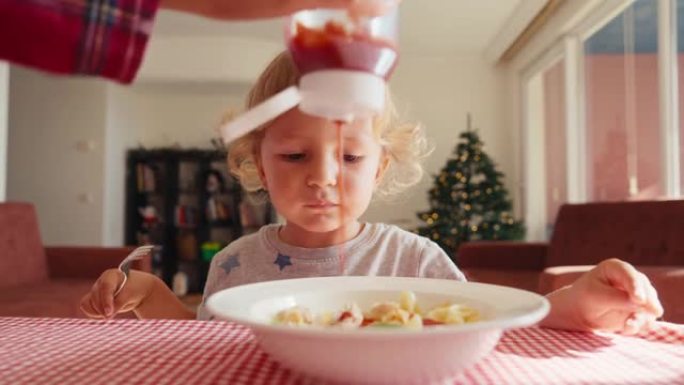 餐桌上厨房里的孩子在吃番茄酱通心粉。母亲给孩子加番茄酱。不良饮食习惯