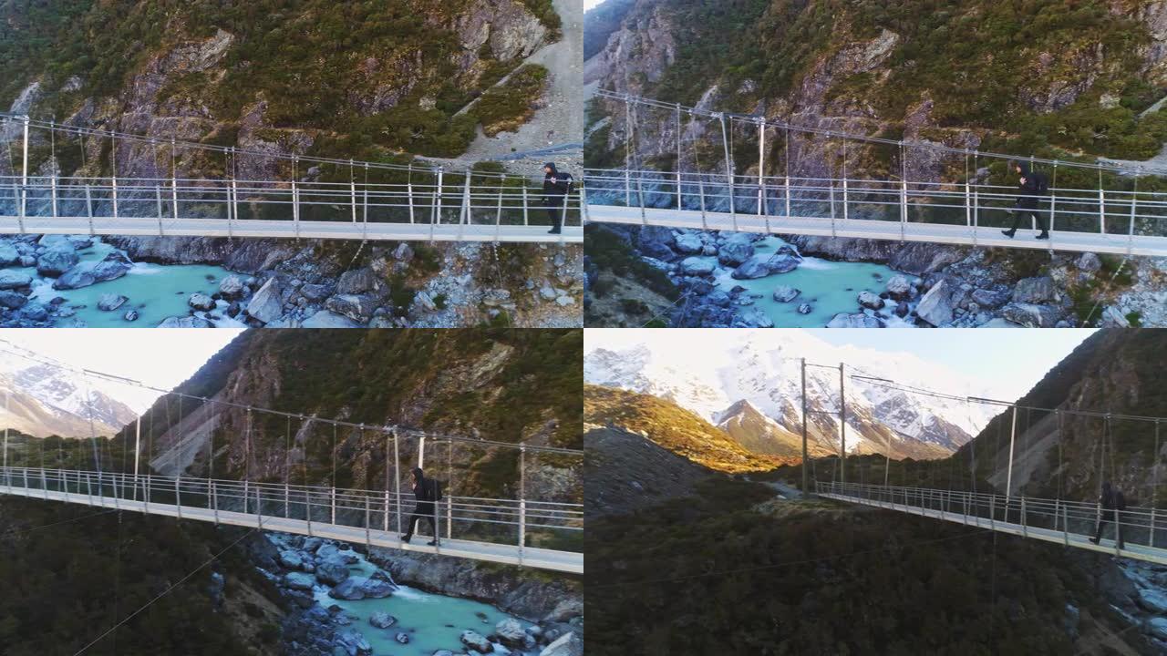 徒步旅行者沿着悬索桥漫步，冲向急流的河水，到达雪山