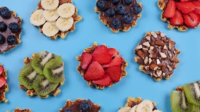 旋转背景的开胃的甜威化饼与巧克力酱，坚果和水果在蓝色的背景。夏天，明亮，新潮背景，美食设计