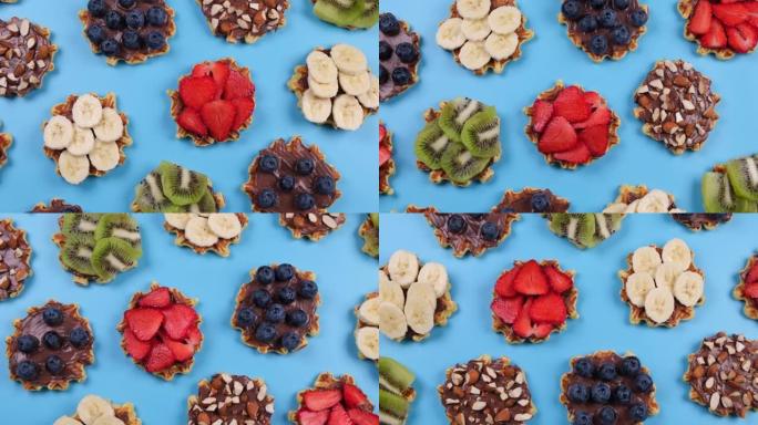 旋转背景的开胃的甜威化饼与巧克力酱，坚果和水果在蓝色的背景。夏天，明亮，新潮背景，美食设计