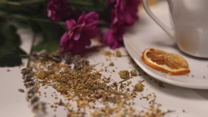桌子上的陶瓷杯茶的特写视图，桌子上放着草药，蜂蜜罐，鲜花