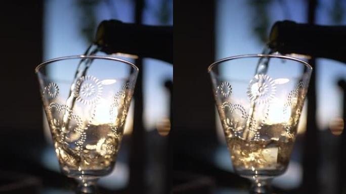 在室外日落时将白葡萄酒倒在玻璃上。垂直视频中提供酒精饮料的慢动作镜头