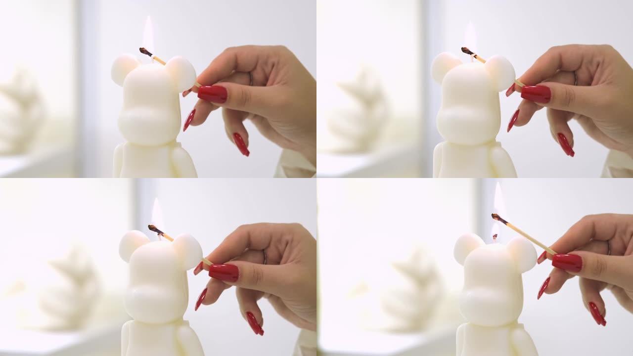 带有红色指甲的女孩特写镜头照亮了熊形状的蜡烛上的灯芯。手工蜡烛的制造