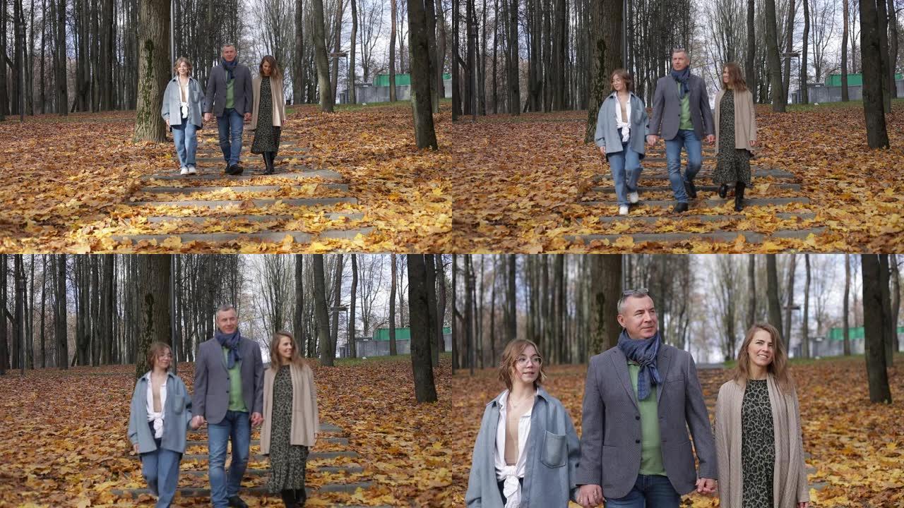 幸福的一家三口在森林里沿着黄叶环绕的台阶向前走。父母和十几岁的孩子在秋天的公园散步。自然景观优美，落