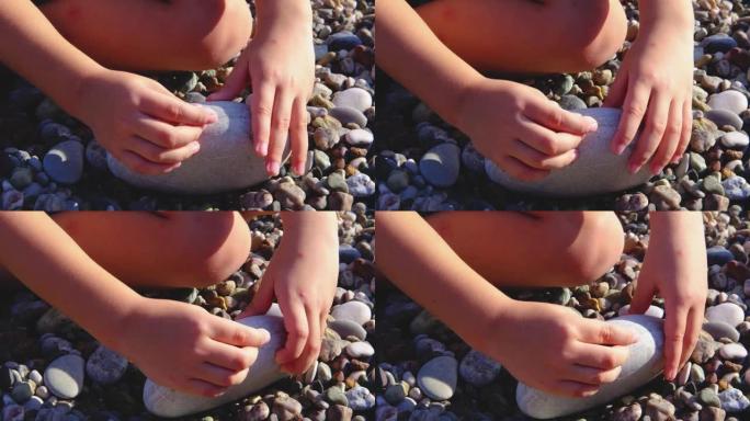 一个孩子在沙滩上玩石头特写。