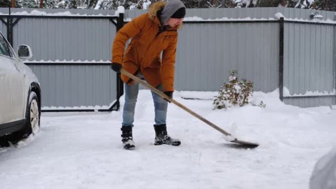 一个冬天的人在停车场的一所房子的院子里用铁锹扫雪。降雪天气条件恶劣汽车熄火挖开通道