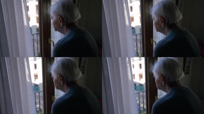 沮丧的孤独的高加索老妇人站在阳台的门口，看着夏天的街道。悲伤的高级女性退休人员想独自在家度过一天。
