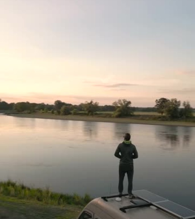 傍晚，一名男子站在露营车顶上，欣赏着河上的景色
