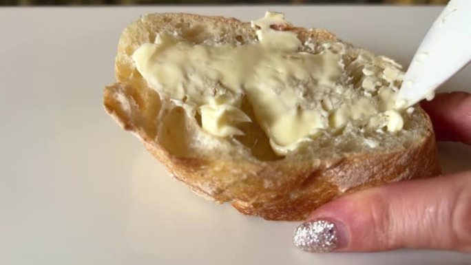 女性手与闪亮的美甲涂抹三明治与黄油在白面包法国面包ciabatta不出来整齐涂抹黄油涂抹在各个方向白