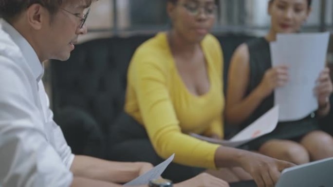 一群多种族的人在用笔记本电脑和文书工作开会。
