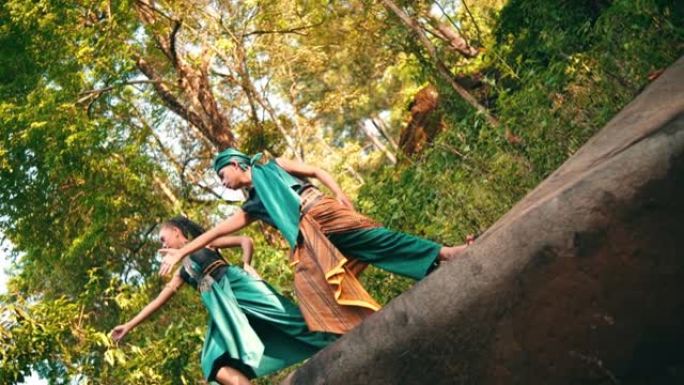 一名亚洲男女在森林中央穿着绿色衣服在岩石上跳舞