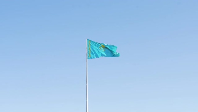 在阳光明媚的日子里，哈萨克斯坦国旗迎风飘扬。在哈萨克斯坦的蓝天下，旗杆上挥舞着国旗