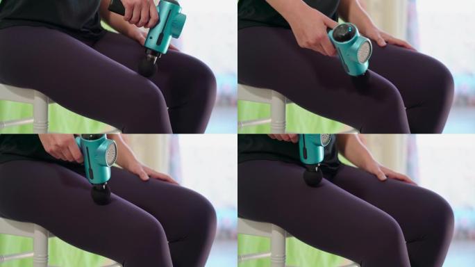 女运动员使用现代按摩枪治疗大腿放松。训练后运动恢复的概念。特写