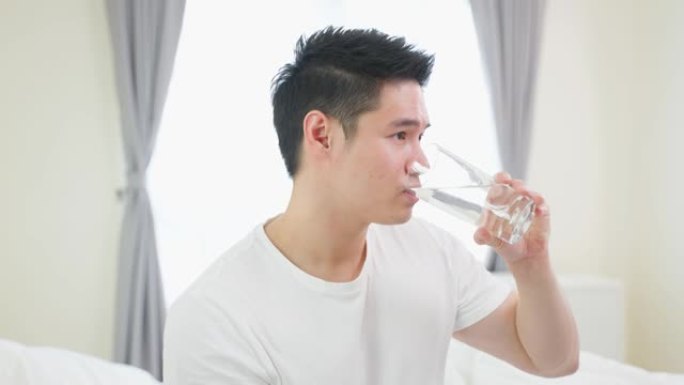 亚洲活跃强壮男子在卧室里拿着干净的水的肖像。有吸引力的口渴的男性饮料，或在醒来后喝一口天然矿物质，以