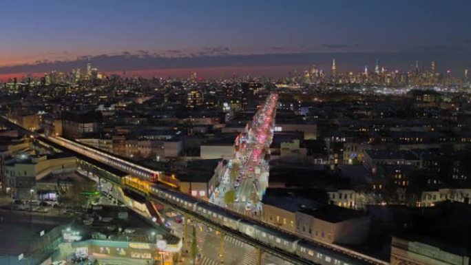 两列火车正经过布鲁克林布什威克的高架地铁车站，曼哈顿天际线的远程景色在夜间照亮。无人机航拍视频与后摇