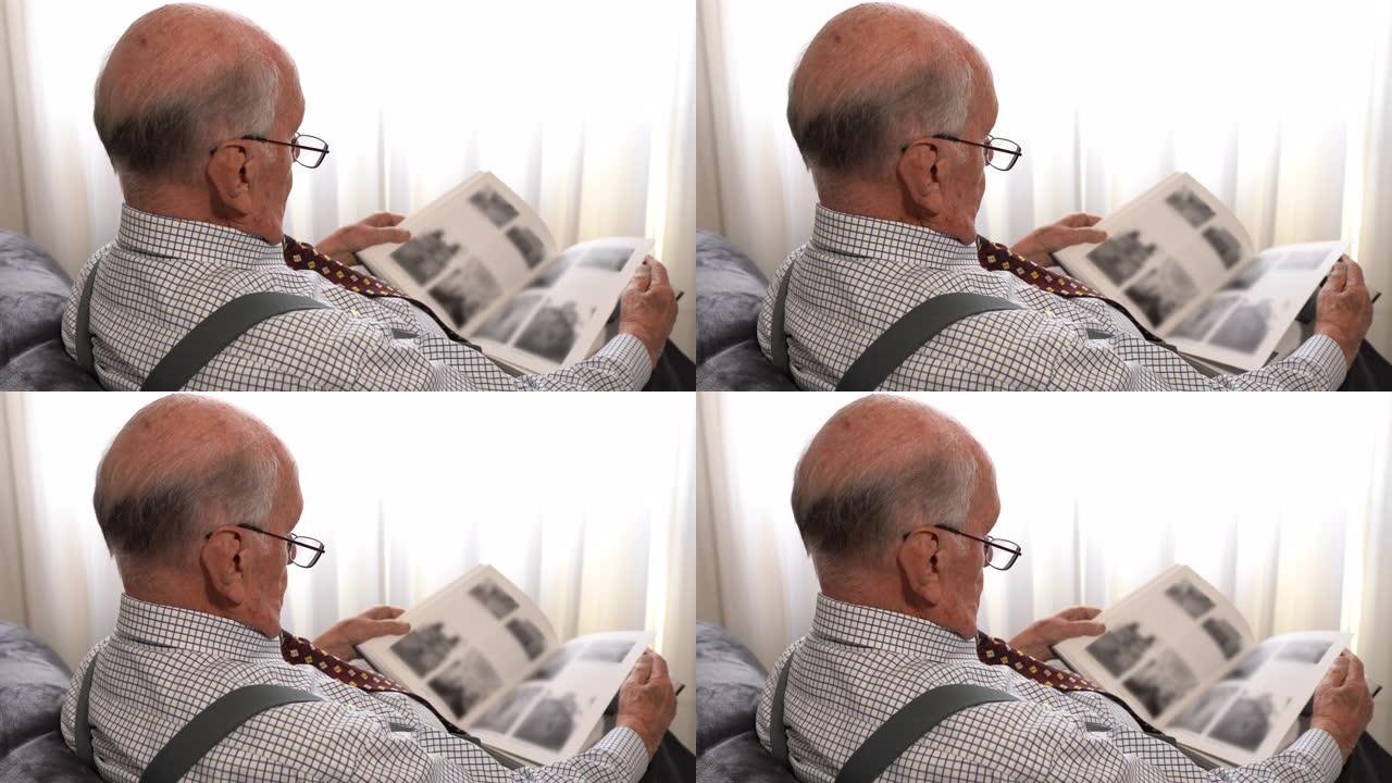 退休老人的后视镜头花时间在家中阅读文学，建筑或历史书籍，戴眼镜和领带的优雅老人看着书中的黑白模糊图像