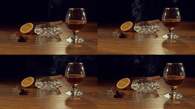 雪茄在一杯威士忌，橙子和巧克力棒附近的烟灰缸上慢慢燃烧