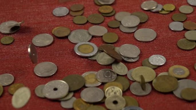 各种硬币落在一堆硬币旁边的红色表面上，慢动作