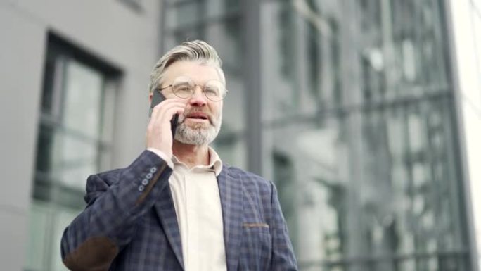 戴着眼镜的英俊成熟商人在现代商业中心工作电话交谈穿着经典西装的成功男人企业家