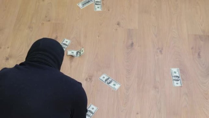 一个戴着黑色巴拉克拉瓦帽的男人从地板上捡起美钞。强盗对赃物很满意