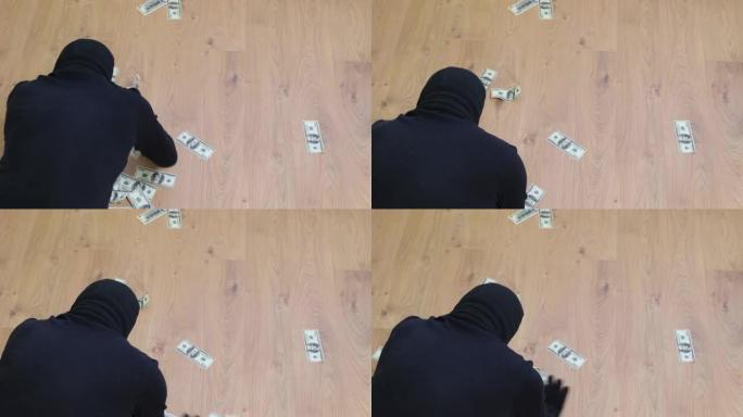 一个戴着黑色巴拉克拉瓦帽的男人从地板上捡起美钞。强盗对赃物很满意