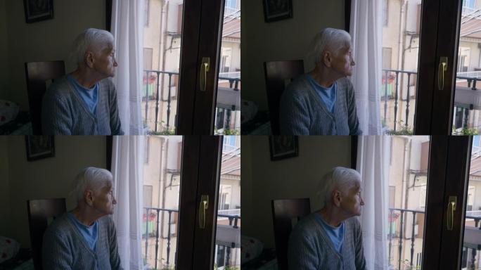 体贴入微的白人老妇人的侧视肖像，看着坐在室内椅子上的阳台门。悲伤沮丧的孤独退休人员在夏天在家。