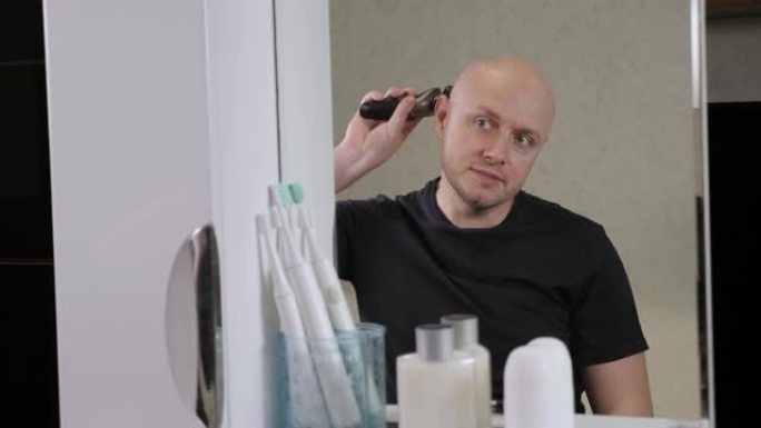 一个秃头男人在浴室里用电动剃须刀剃光头。