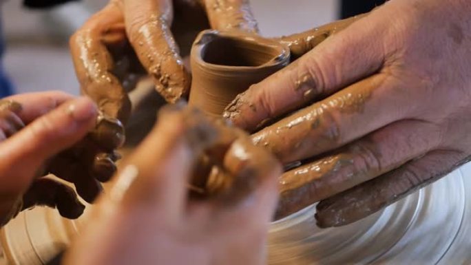 陶工大师的男性手在旋转的陶工轮上创造了粘土kushin的形状，同时在培训车间向十几岁的孩子教授陶艺课