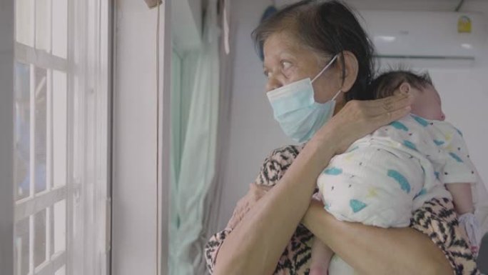 亚洲祖母在家戴口罩抱孙子。