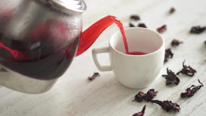 红色饮料是从玻璃茶壶中倒出的。新鲜煮茶配覆盆子，茶配荚果