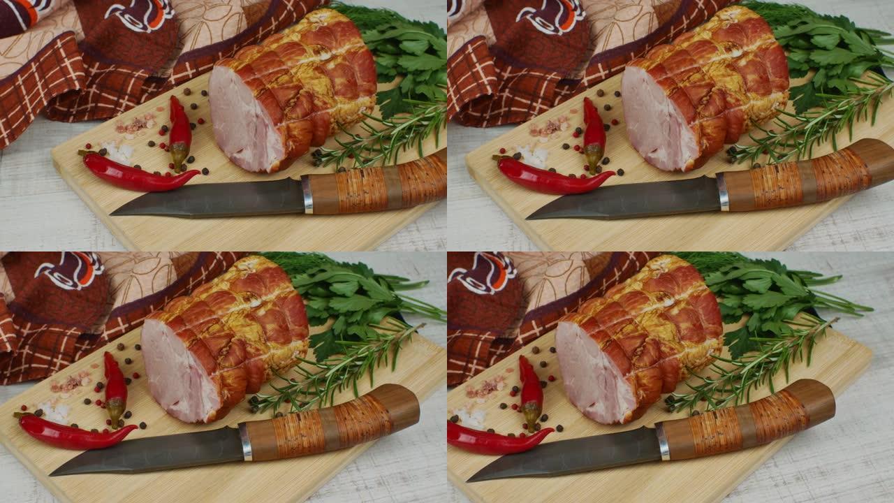 在一块木制砧板上，一块多汁的猪肉火腿，一把雕刻刀，红辣椒，多色多香果，欧芹，莳萝和罗勒。美味猪肉产品