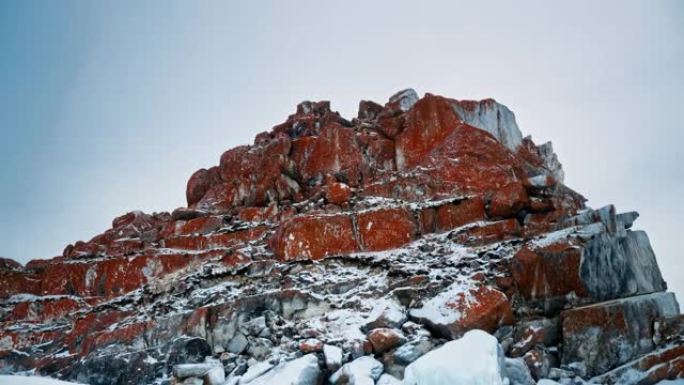 一块红色的岩石，覆盖着红色的地衣，覆盖着雪。俄罗斯西伯利亚贝加尔湖。