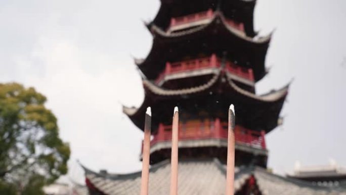 三个燃烧的香棒和烟雾与模糊的上海龙华塔背景在阳光明媚的冬日，4k慢镜头。