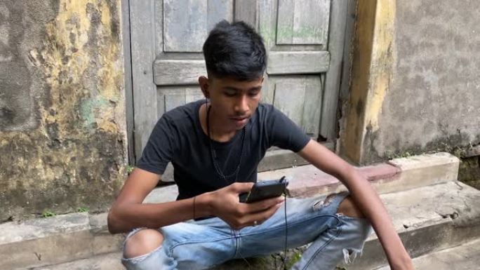 一个年轻的印度男孩穿着黑色t恤和时尚的弯曲牛仔裤坐在台阶前