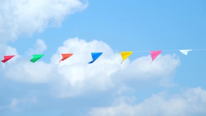 彩色的小旗子在天空中飘扬。在蓝天的映衬下，挥舞着挂在绳子上的小彩旗庆祝节日。