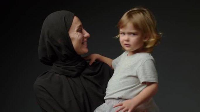 小女孩和她的穆斯林母亲在黑色背景下在家。穆斯林母女在家里一起玩，然后拥抱
