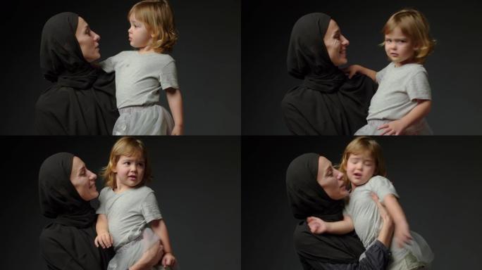 小女孩和她的穆斯林母亲在黑色背景下在家。穆斯林母女在家里一起玩，然后拥抱