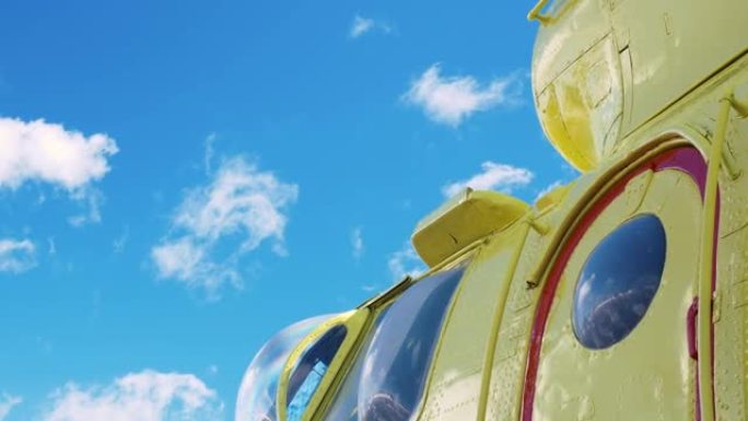 黄色直升机，红色框门，鼓鼓囊囊的窗户。一架亮黄色的直升机映衬着偶尔有小朵云的蓝天。凸窗和直升机水泡。