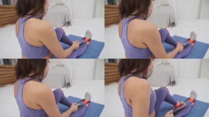 穿着紫色运动服的漂亮女孩正在家里健身。健身女孩用黑色橡皮筋在手部肌肉上锻炼。肩膀的特写。一个健康的女