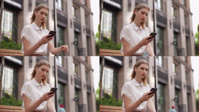 严肃沉思的年轻女子的低角度视角，用打字的手机坐在现代建筑背景的城市街道的长椅上，想着移开视线。