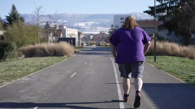 一个年轻超重男子在户外慢跑的背后。追踪一个胖乎乎的男性跑步的照片。回到形状概念