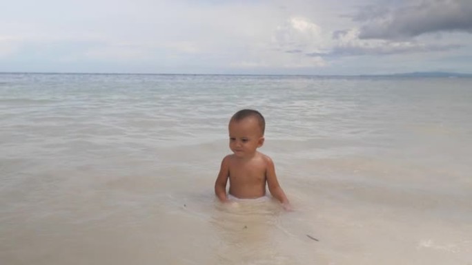 海里的孩子笨拙地走路，在倒下的波浪中跪下。带着婴儿在海上度假。一岁的孩子在水中游泳快乐，玩得开心。为