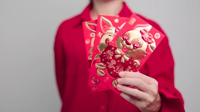 女人拿着装有金兔子和祝福字的中国红包，礼物是春节快乐。中文句子的意思是幸福、健康、幸运和富有