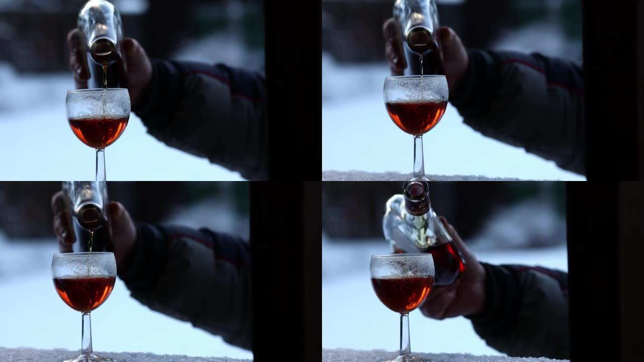 白天在户外，男人的手将白兰地从瓶子里倒入冰霜中的冰玻璃中。寒假。从手上拿走。