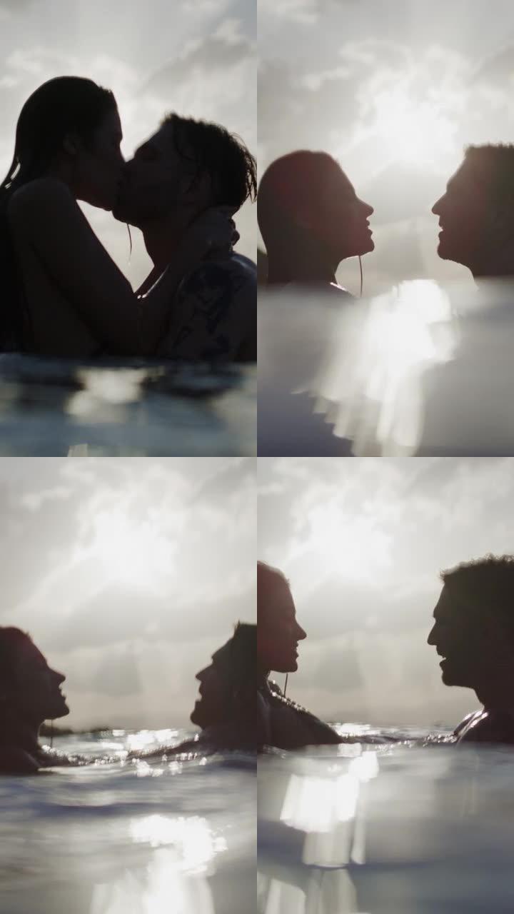 浪漫的异性恋夫妇在美丽的金色日落时在海里游泳。亲吻和拥抱温柔的垂直视频
