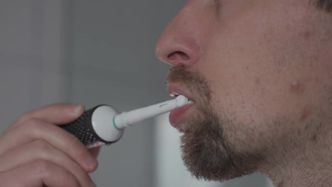 用超声波牙刷清洁牙齿的人的特写。男性用电牙刷刷牙。主题口腔健康和牙齿卫生。浴室里的早上卫生程序。