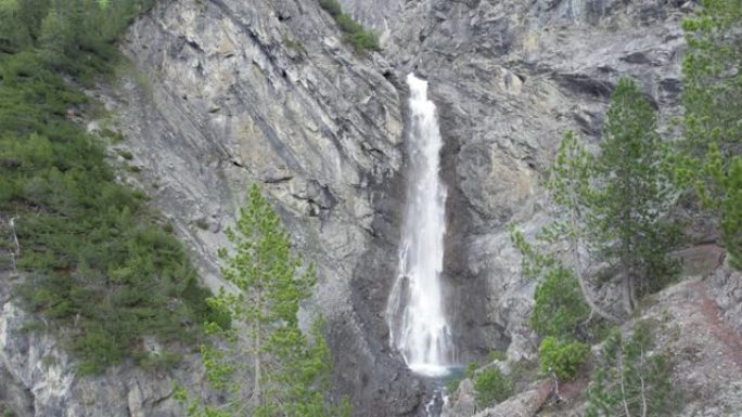 空中无人机镜头在树冠上方缓慢飞行，露出陡峭的瀑布，瀑布从陡峭的山崖边缘飞入瑞士的跳水池。